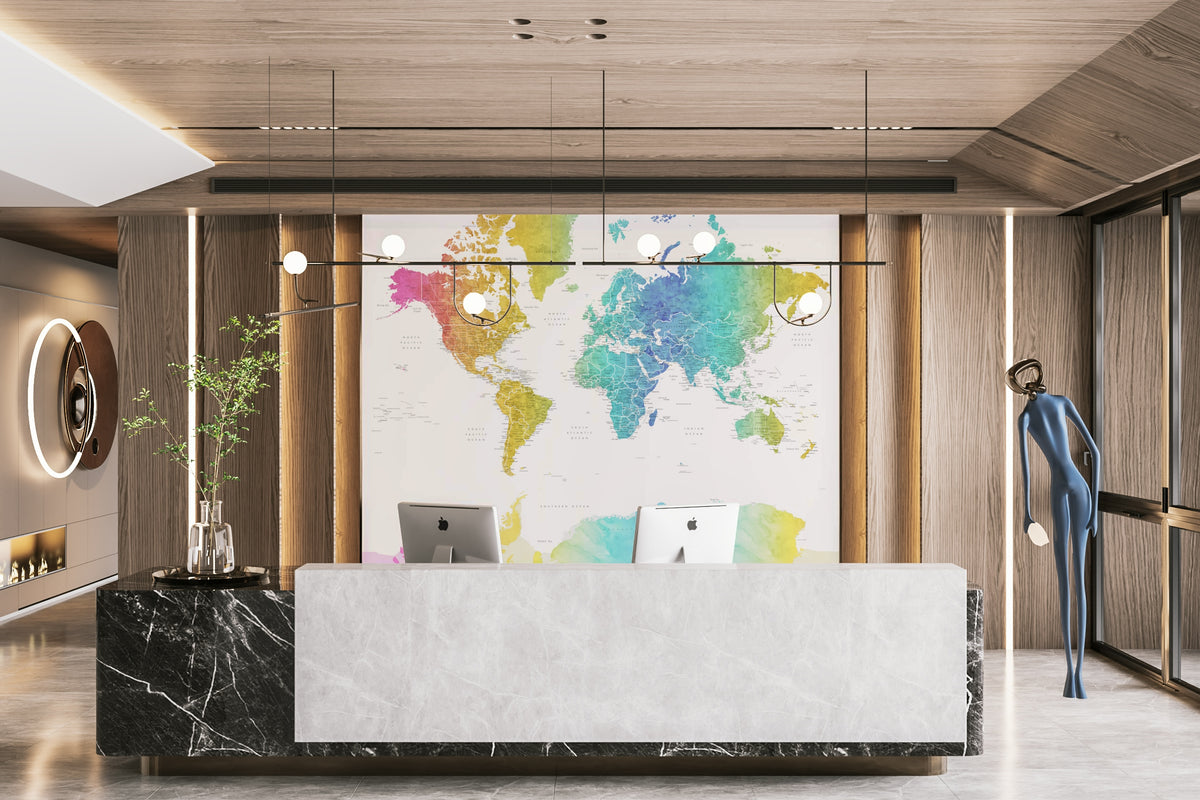 Rainbow World Map wallpaper in bright watercolor behind a white marble reception desk with two iMacs in an office lobby