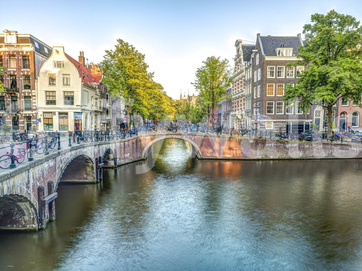 Visit Amsterdam wallpaper mural shown as a full-wall view of a stone canal bridge and Dutch houses by the water
