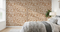 Earth toned shapes wallpaper behind a bed with grey bedding and a macrame throw GD12478