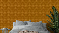 Amber Hues wallpaper in warm mustard tones above a grey quilted bed beside a green ZZ plant in a bedroom