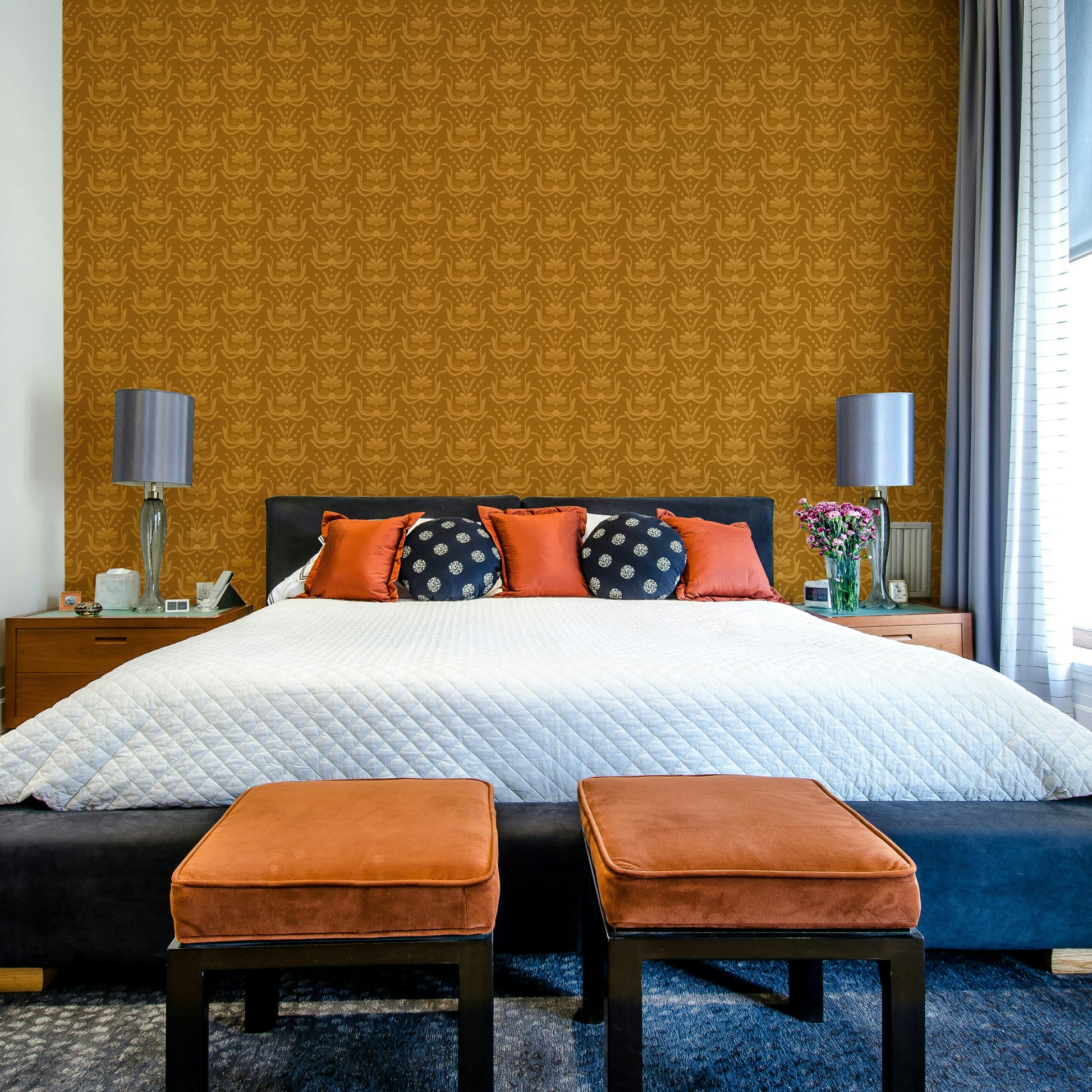Amber Hues wallpaper in mustard tones above a black bed with orange cushions and ottoman benches