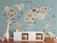 Animal Adventure Atlas wallpaper mural in sage green behind a white console with woven baskets and a plush giraffe in a kids room