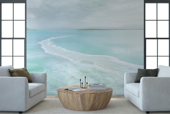 Aqua Calm wallpaper mural of a turquoise sea and pale shoreline behind two white armchairs and round wood table