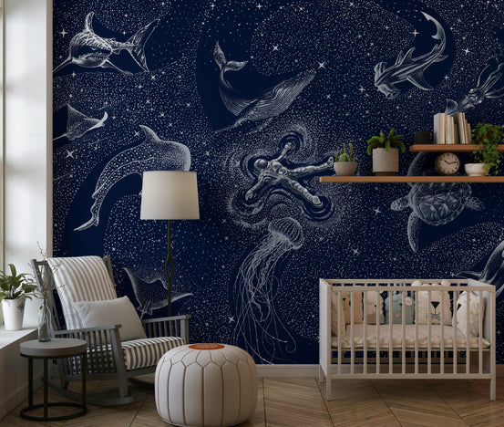 Astral Sea wallpaper mural with navy starry sky and white sea creatures behind a white crib and rocking chair in a nursery