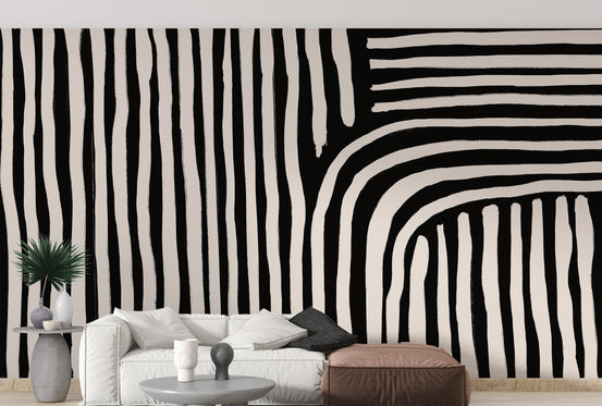 Black and white striped wallpaper mural of wavy painted lines behind a white sofa and brown pouf in a living room