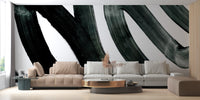 Black Brush Stroke wallpaper mural with bold black painterly swirls on white behind a beige and grey sofa in a living room