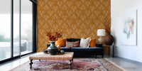 Boho Art Nouveau Folk Floral Mustard Gold wallpaper behind a navy sofa and woven ottoman in a bright living room