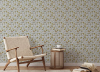 Buttercups Garden Golden and Gray wallpaper behind a woven rattan armchair and caned side table