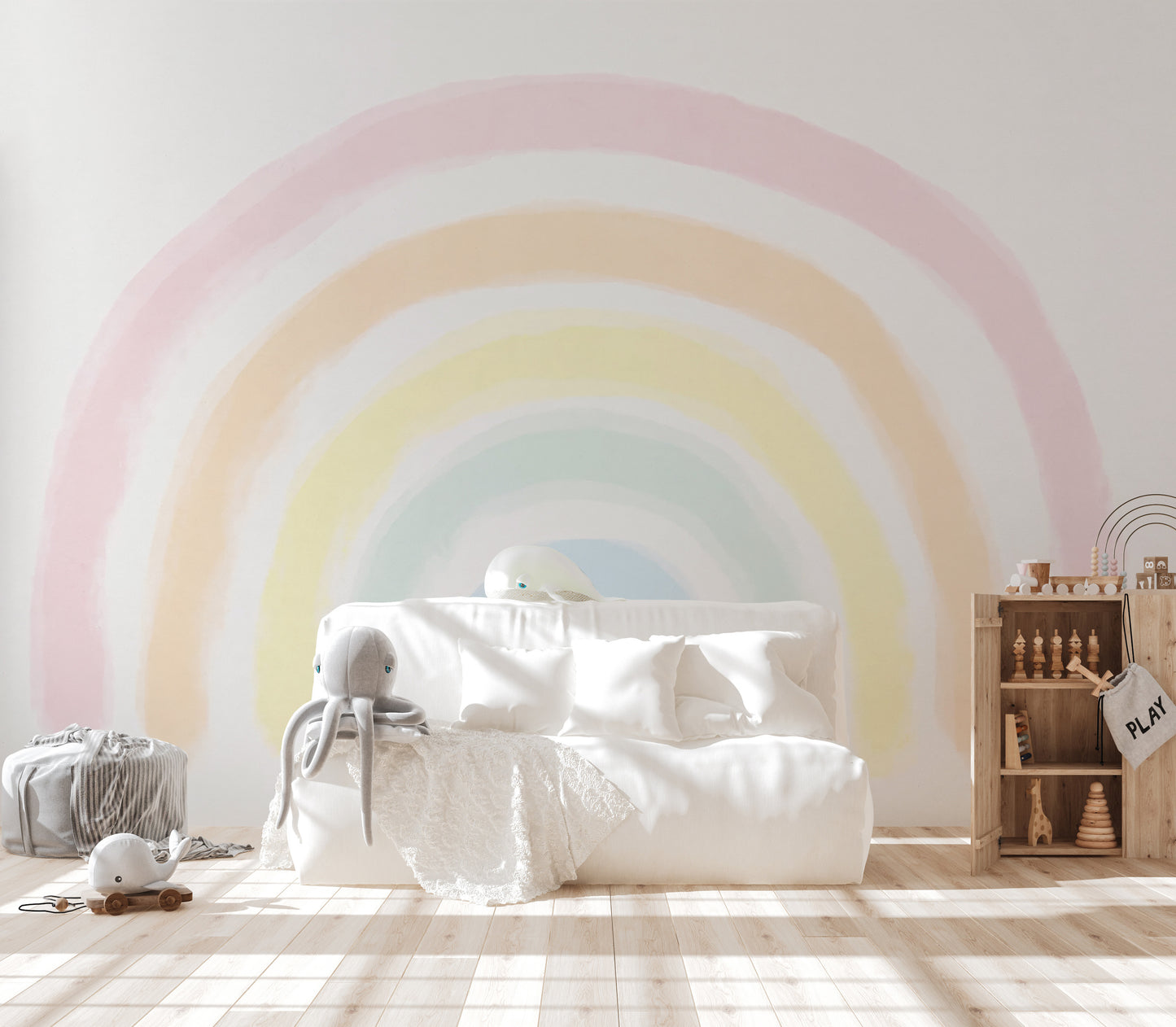 Pastel Rainbow wallpaper mural behind a cozy white daybed with whale plush toys in a bright kids playroom