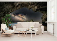 Cave Portal to Starlight wallpaper mural of a galaxy in a dark cave behind a cream sofa and rattan chair in a living room