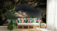 Cave Portal to Starlight wallpaper mural of the Milky Way in a dark cave behind a rattan sofa in a tropical living room