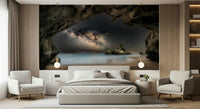 Cave Portal to Starlight wallpaper mural of the Milky Way in a sea cave above a gray bed and armchairs in a bedroom
