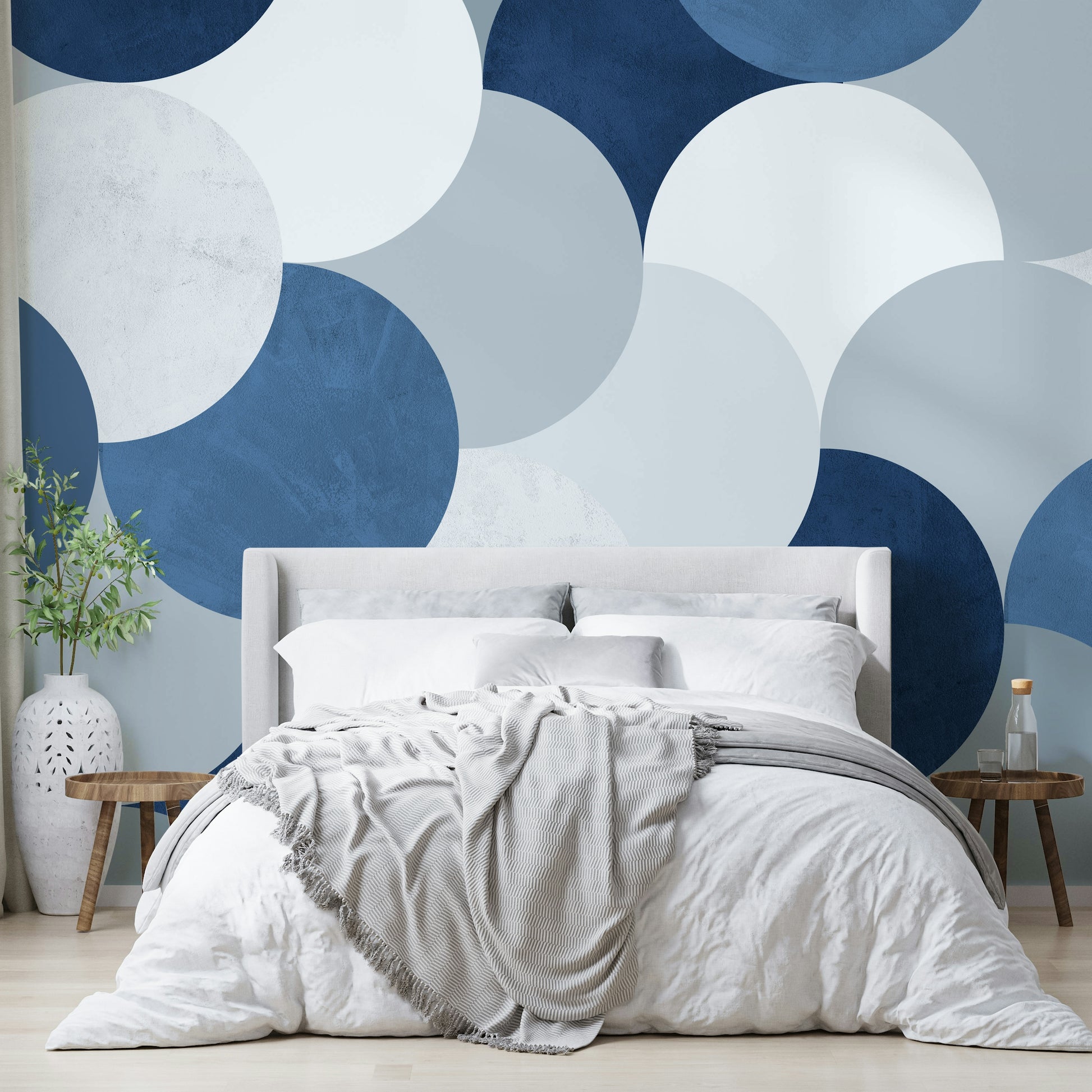Circle Abstract wallpaper mural with navy and white circles behind a cream upholstered bed and gray throw