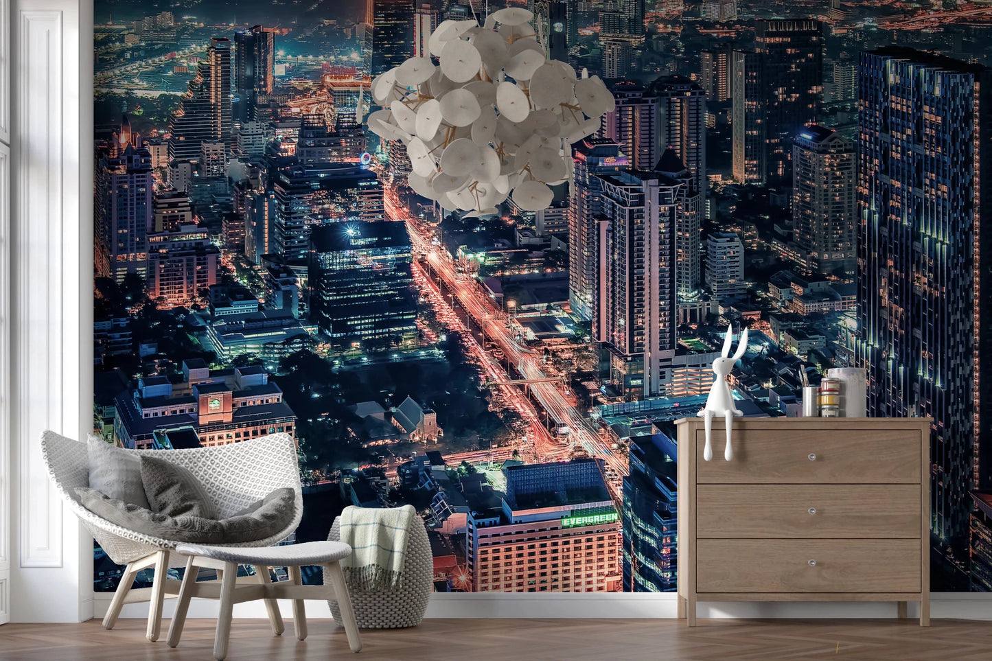 Cityscape Night wallpaper mural with glowing city lights behind a gray armchair and wood dresser in a living room