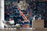 Cityscape Night wallpaper mural with glowing city lights behind a gray armchair and wood dresser in a living room