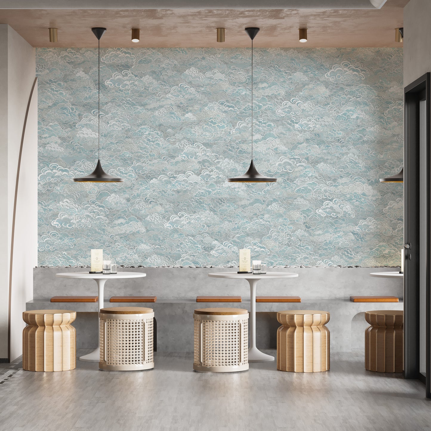 Clouds Baby Blue and White cloud-pattern wallpaper mural above concrete bench seating and rattan stools in a cafe