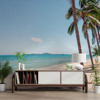 Coastal Palm Serenity wallpaper mural of turquoise sea and palms behind a wood credenza styled with books and a lamp