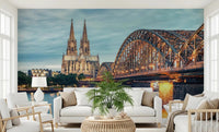 Cologne at Dusk wallpaper mural with the cathedral and Hohenzollern Bridge behind a white sofa and armchairs in a living room