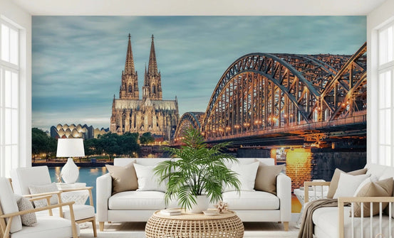 Cologne at Dusk wallpaper mural with the cathedral and Hohenzollern Bridge behind a white sofa and armchairs in a living room