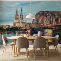 Cologne at Dusk wallpaper mural with the cathedral and glowing bridge behind an oval dining table and beige chairs