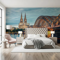 Cologne at Dusk wallpaper mural of the cathedral at twilight above a tufted bed and pink accent chair in a bedroom