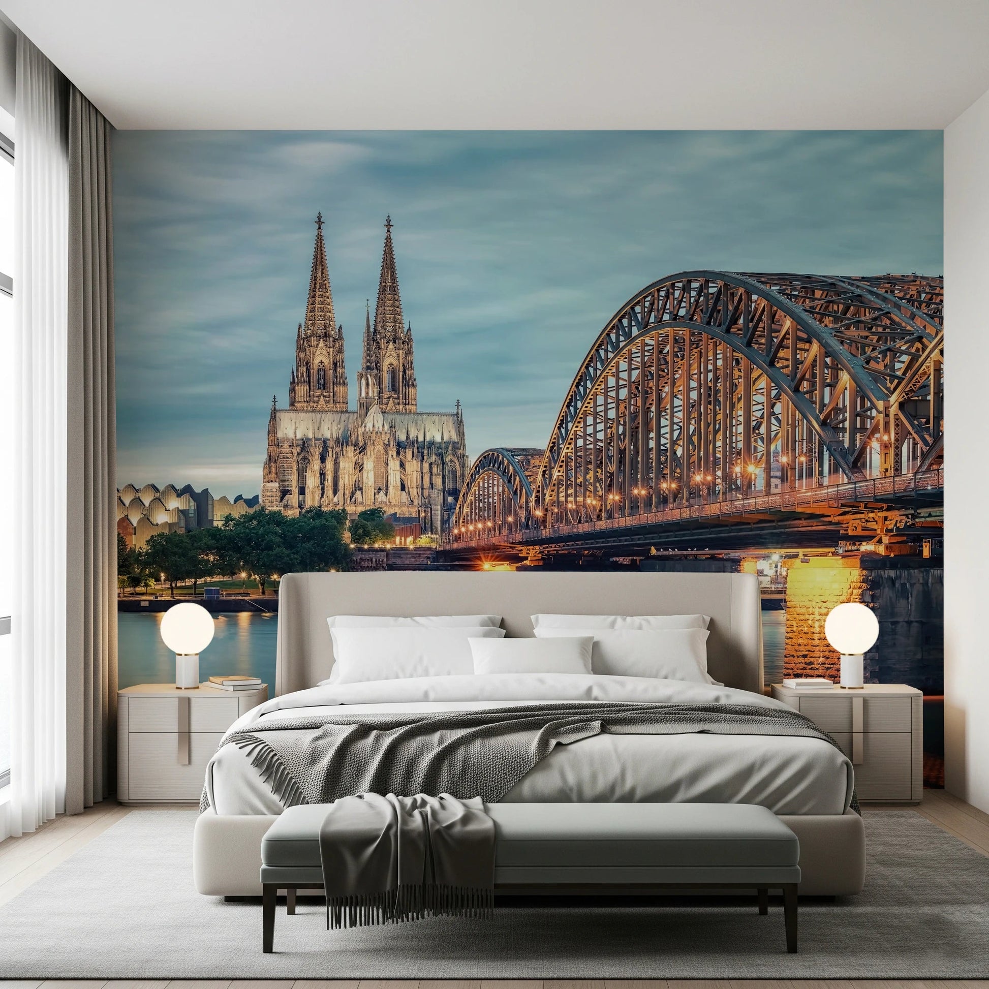 Cologne at Dusk wallpaper mural with the cathedral and amber-lit bridge above an upholstered bed flanked by globe lamps