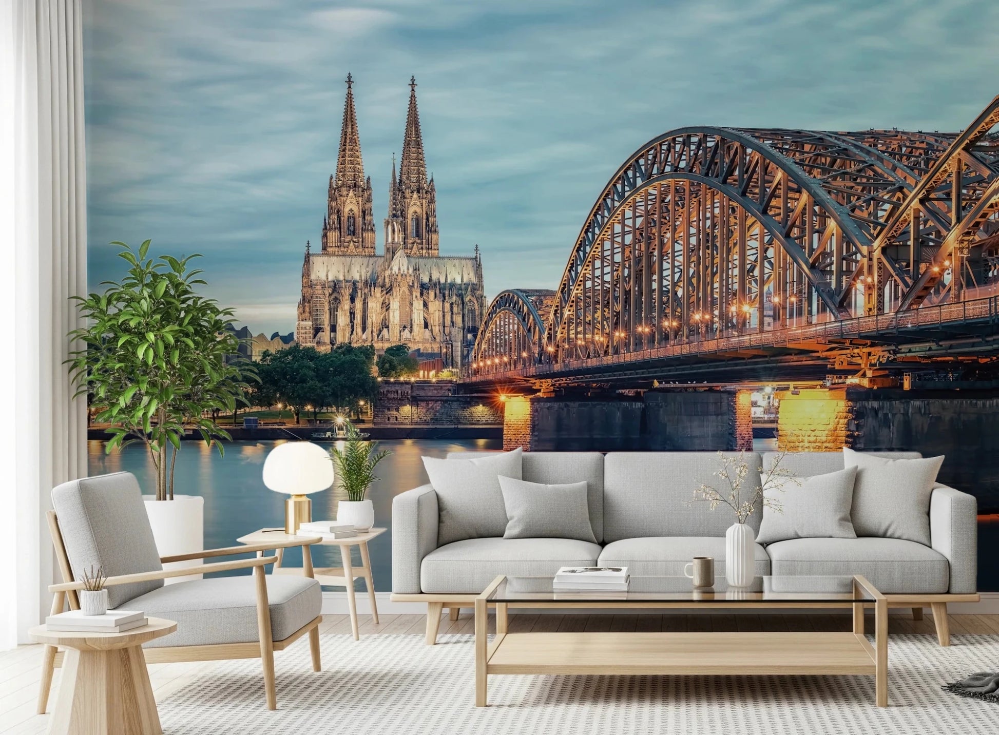 Cologne at Dusk wallpaper mural showing the illuminated bridge and cathedral behind a grey sofa and armchair in a living room