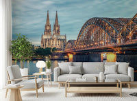 Cologne at Dusk wallpaper mural showing the illuminated bridge and cathedral behind a grey sofa and armchair in a living room