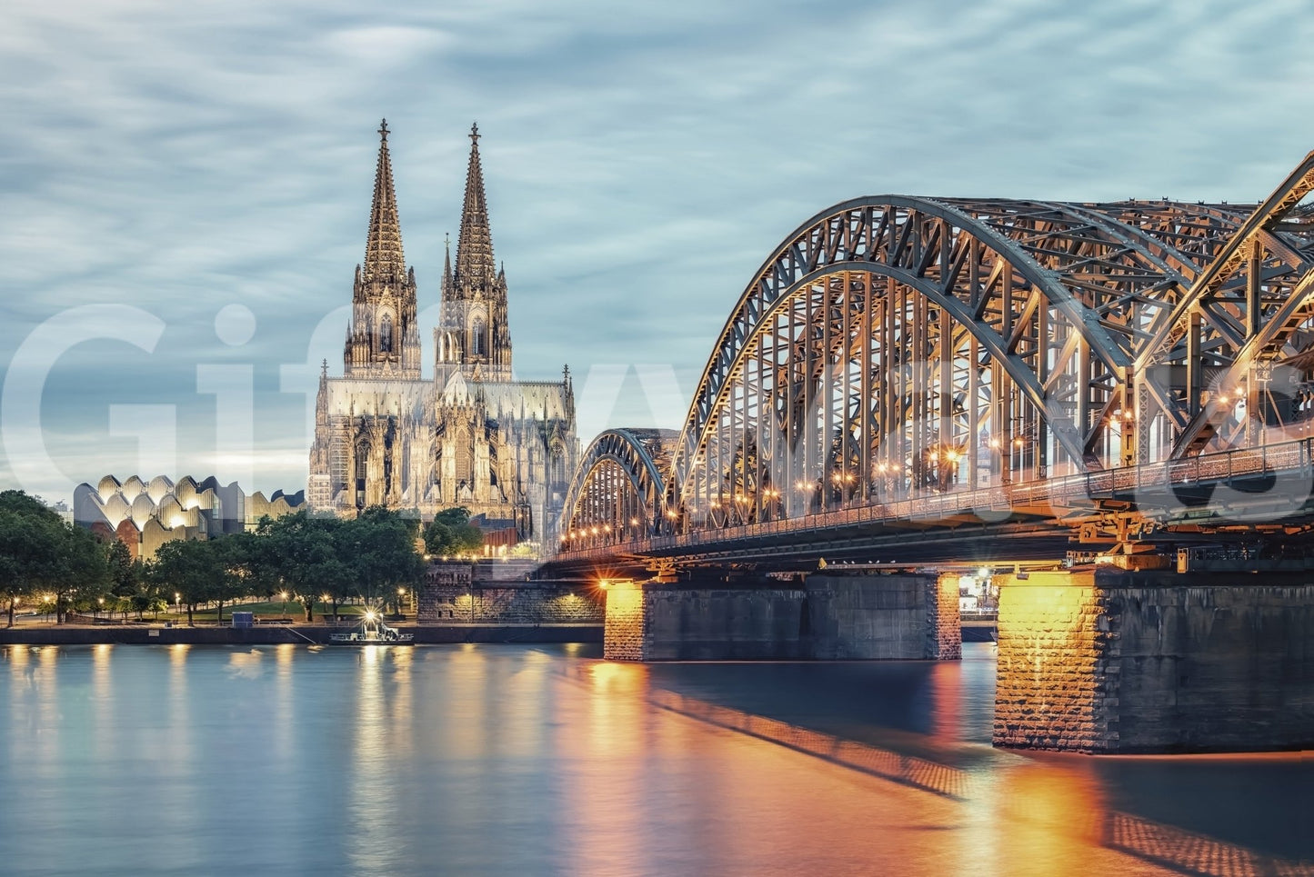 Cologne at Dusk wallpaper mural close-up showing the lit cathedral spires and Hohenzollern Bridge glowing over the Rhine at dusk