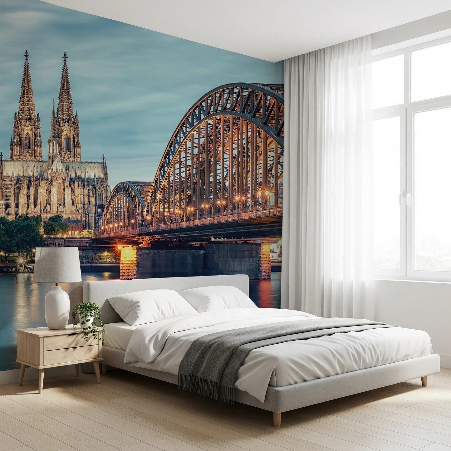 Cologne at Dusk wallpaper mural showing the steel bridge and cathedral behind a white bed and nightstand in a bright bedroom