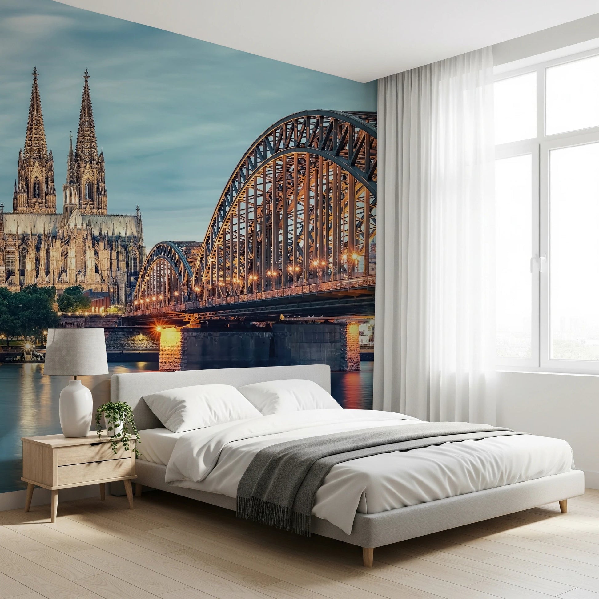 Cologne at Dusk wallpaper mural showing the steel bridge and cathedral behind a white bed and nightstand in a bright bedroom