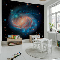 Cosmic Symphony wallpaper mural with a spiral galaxy in a kids room with a white play kitchen, table and chairs