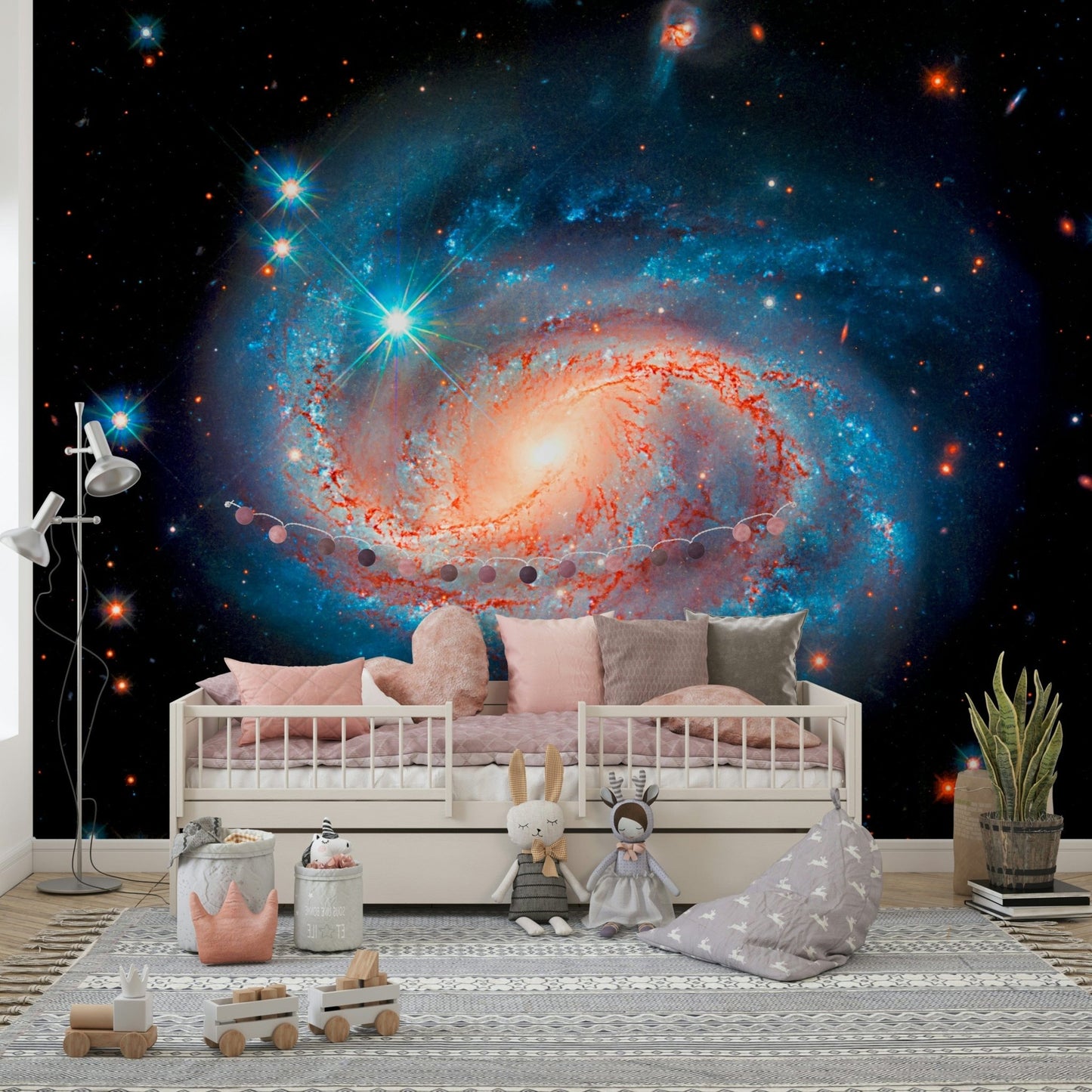 Cosmic Symphony wallpaper mural with a glowing spiral galaxy above a pink crib in a kids room with bunny toys