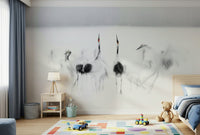 Crane Dance in White wallpaper mural of ink-wash cranes behind a child's bed with blue bedding and teddy bear