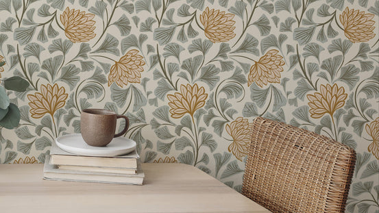 Dancing Bloom wallpaper with mustard florals and sage leaves behind a stacked books and brown mug on a wood desk