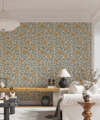 Dancing Bloom wallpaper with amber blooms and sage leaves behind a wood bench, white sofa and table lamp in a living room