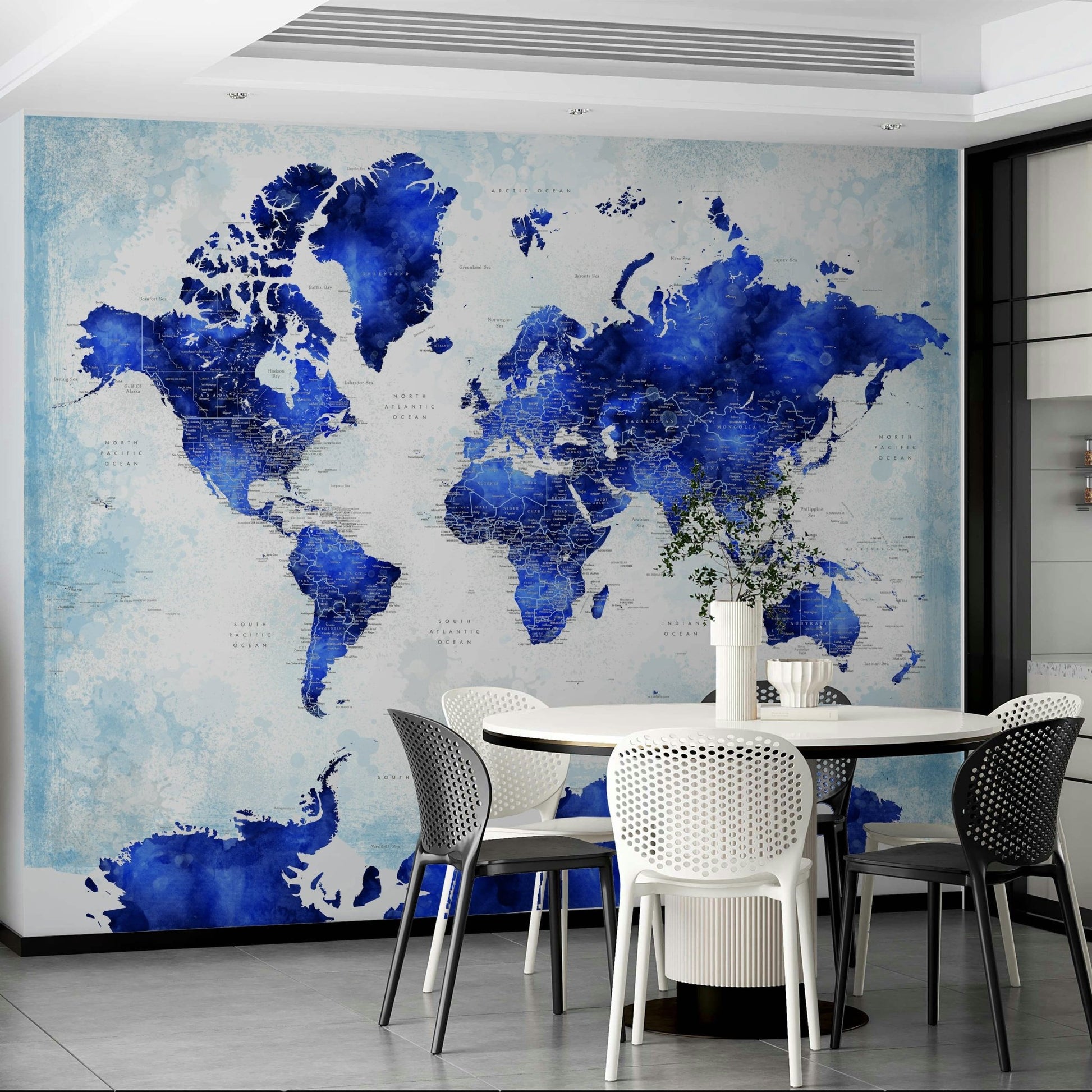 Deep Blue Watercolor World Map wallpaper behind a round white dining table with white and black chairs