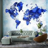 Deep Blue Watercolor World Map wallpaper above a mint green chesterfield sofa and tan egg chair in a lounge