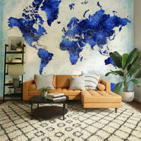 Deep Blue Watercolor World Map wallpaper above a tan leather sectional sofa with a ladder shelf and palm