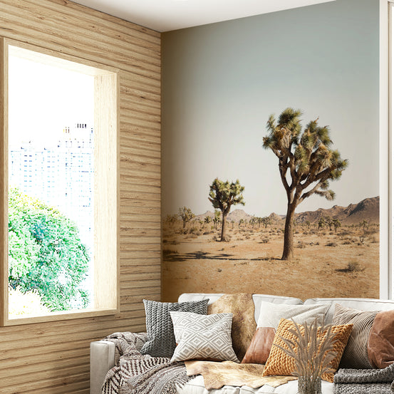 Desert Tree wallpaper mural with Joshua trees behind a beige sofa and patterned pillows in a wood-panelled living room
