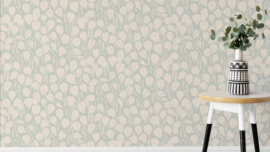 Dewy Birch Branches wallpaper in sage green behind a round stool with a striped vase and eucalyptus