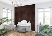 Dirty Paper Cognac wall mural in deep brown in a music room with white upright piano between bright windows