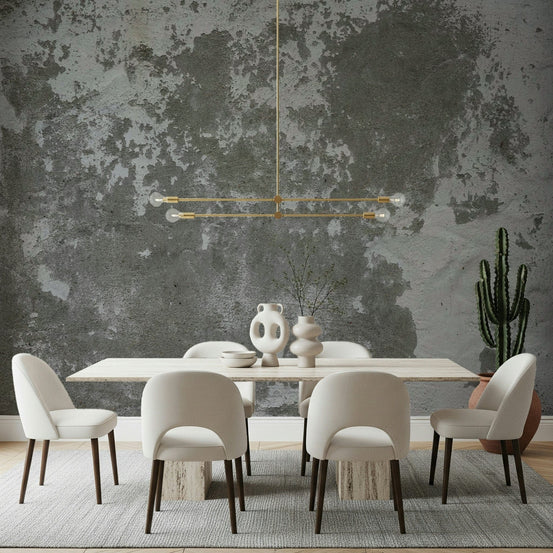 Distressed wallpaper mural in weathered grey concrete behind a travertine dining table with cream chairs and brass chandelier