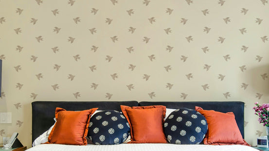 Dreamy Birds Summer Sand wallpaper with taupe bird silhouettes behind a navy headboard with rust and polka-dot cushions in a bedroom