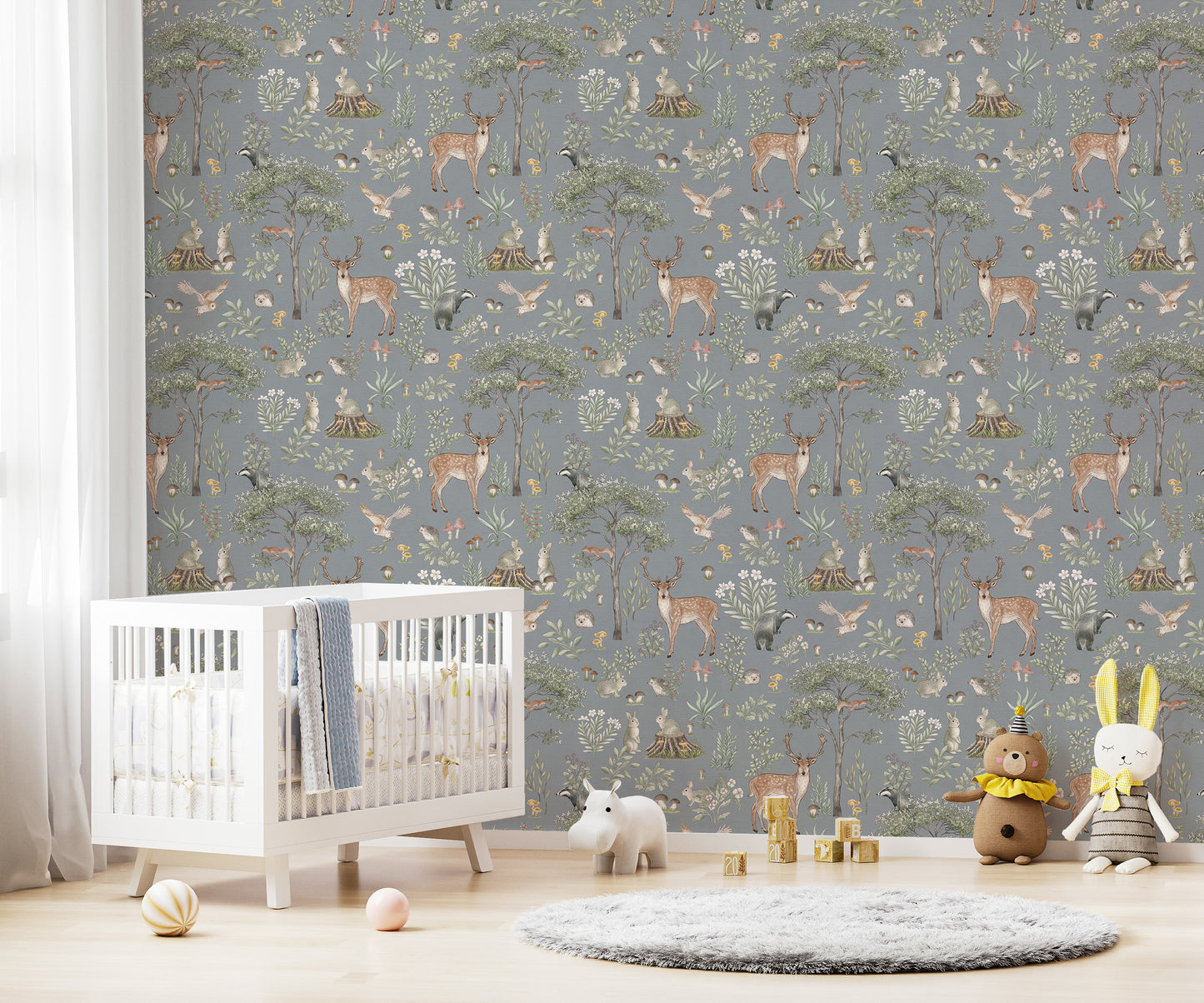 Dusty Blue Wildlife wallpaper in a nursery with a white crib, teddy bear and bunny plush toys