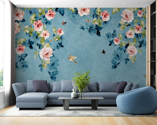 Watercolor Pink Roses on Blue-Green wallpaper with cascading roses and birds behind a blue-gray sofa in a living room