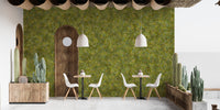 Embroidery Moss Green Color wallpaper mural covering a cafe patio wall with white chairs, wood tables and potted cacti