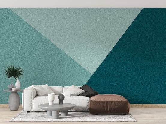 Emerald and Cyan Geometric wallpaper in teal triangles behind a white sofa and brown leather ottoman in a living room