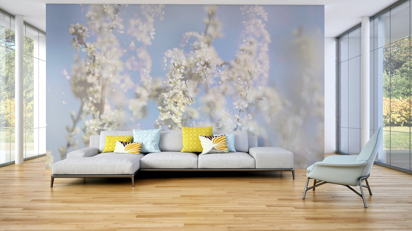 Ethereal Blossom Photography soft white floral wall mural behind a gray sofa with yellow pillows in a glass-walled living room