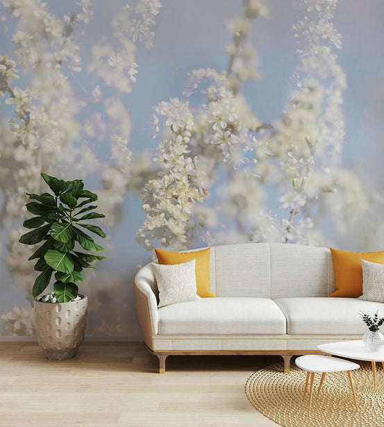 Ethereal Blossom Photography soft white floral wall mural behind a cream curved sofa with orange pillows in a living room